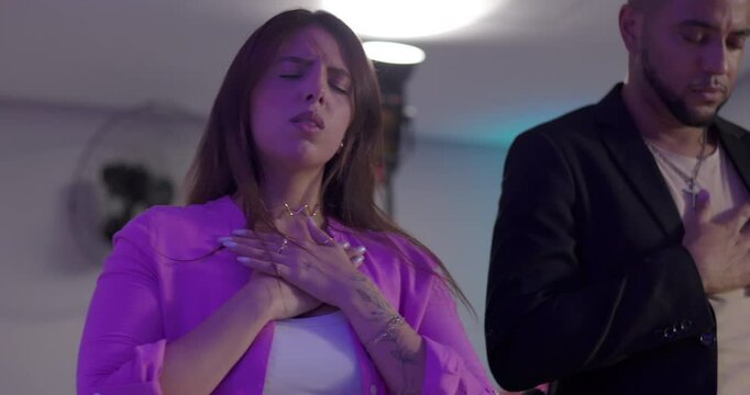 Latin woman with hand on chest and eyes closed during evangelical worship, expressing devotion and faith with emotional sincerity in church service