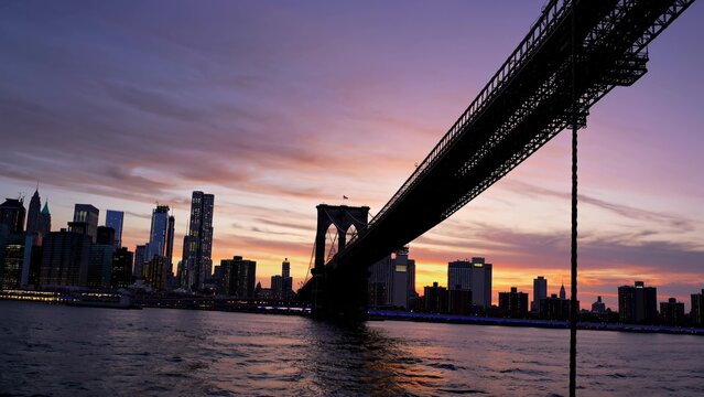 The iconic brooklyn bridge stretches across the east river at sunset, with the illuminated manhattan skyline creating a breathtaking urban panorama
