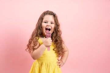 Cute girl with yellow dress and microphone singing on pink background.