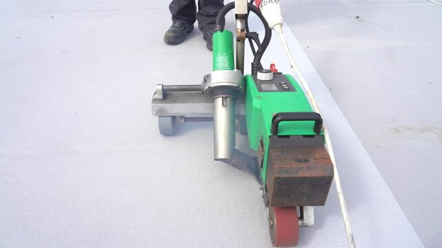 A worker welds a PVC membrane with a heater using a welding machine on the roof of a building. Roofing works.