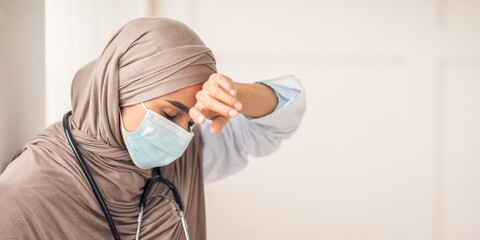 Stressed muslim woman doctor in protective face mask touching her sweating forehead, feeling...