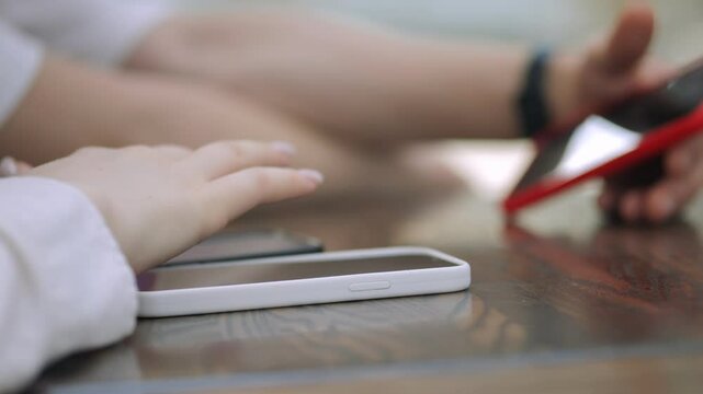 Person is using a cell phone while another person looks on. The scene is casual and relaxed, with the two people sitting at a table