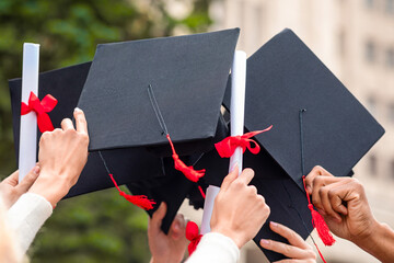 Graduation hats and diplomas raised up in students hands over university or college building,...