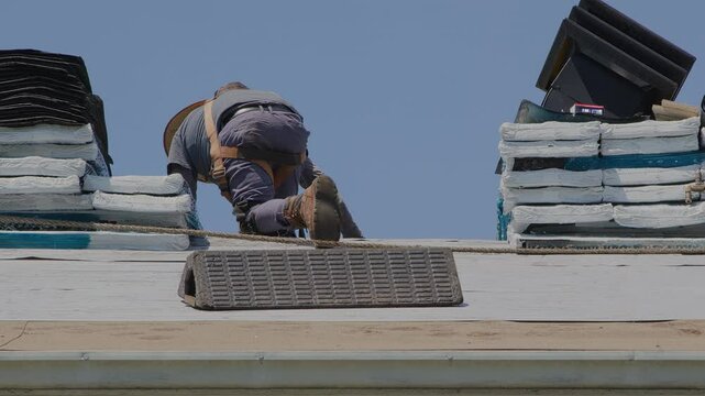 Professional Roofer Installing Asphalt Shingles on Residential House Roof Under Blue Sky
