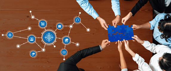 A diverse team of professionals collaborates over a puzzle symbolizing strategic planning, surrounded by digital icons that represent modern business connections and teamwork. Amity