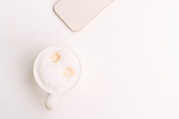 Top view of cappuccino with two espresso spots and beige phone on a white surface. High quality photo
