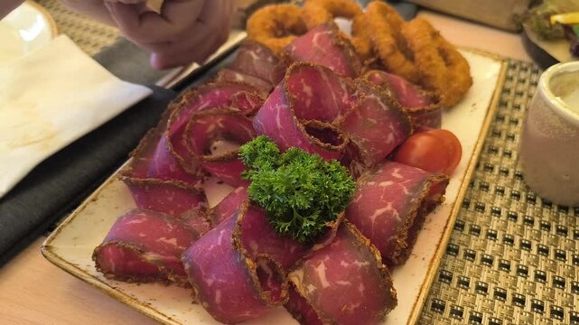 thinly sliceda hand takes thinly sliced ​​basturma from a plate ​​basturma lies on a plate