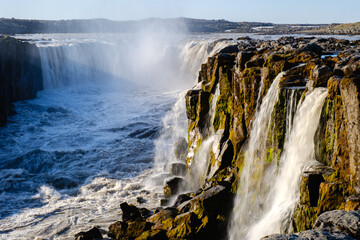 Majestic Dettifoss waterfall showcases powerful cascades as sunlight illuminates the rugged cliffs....