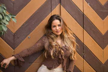 Young, beautiful woman, brown hair, wearing a brown shirt and light pants, posing looking at the...