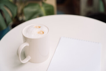Ceramic cup filled with coffee on a round table next to an open notepad. High quality photo