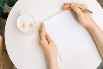 Flat lay with coffee, notebook, and womans hands holding a pen, seen from above. High quality photo
