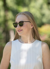 A woman wearing sunglasses and a white shirt with black stripes. She is smiling and looking at the camera