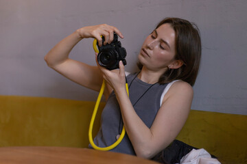 A young woman is holding a camera and looking around at a table in a cafe.