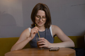 Young woman in glasses sitting with orange coffee in a cozy cafe