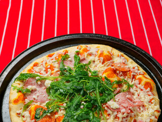 A pizza with ham and spinach on a black tray. The pizza is sitting on a red and white stripe table...
