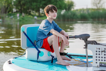 A boy swims on a sup board on a lake. Summer water activities. Electric sapboard
