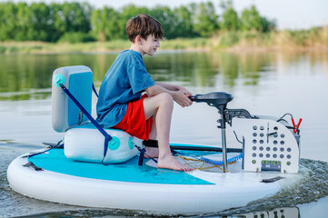 A boy swims on a sup board on a lake. Summer water activities. Electric sapboard