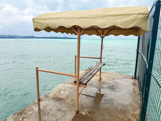 Old wooden bench with yellow canopy on waterfront pier under cloudy sky, evoking solitude, reflection, and travel inspiration