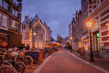 Nighttime Amsterdam. The city is illuminated with various lights. An empty street, with apartment buildings and parked bicycles.