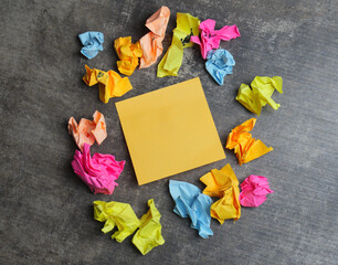 Crumpled papers in various colors are arranged around a blank sticky note