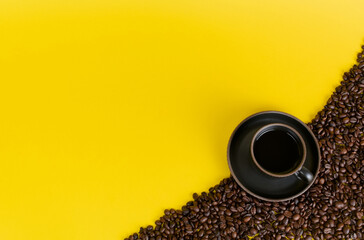 Black coffee cup resting on roasted coffee beans on yellow background