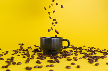 Roasted coffee beans falling into black cup on yellow background