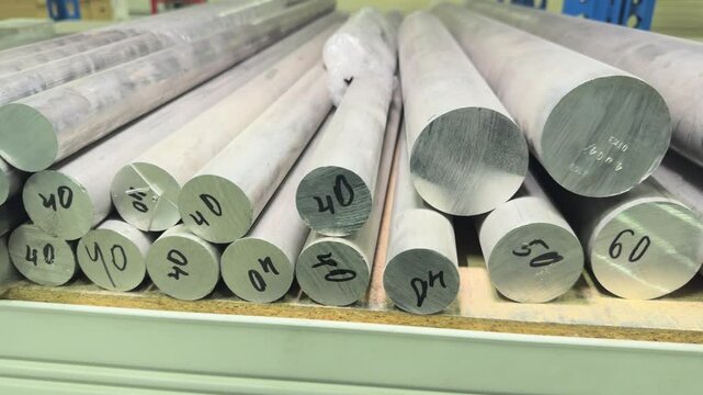 Round billets of different diameters made of aluminum alloy lie on a rack in the warehouse of the metalworking workshop