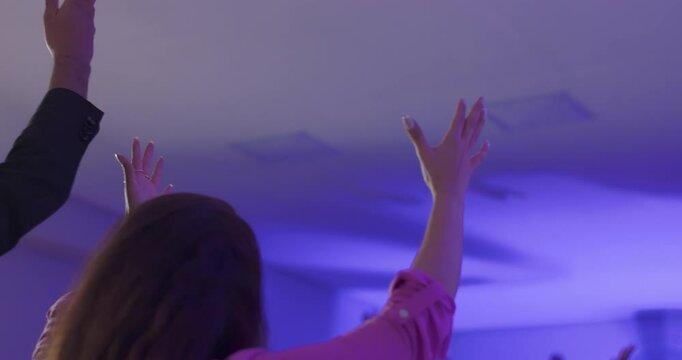 Rear view of Latin woman raising arms in worship during evangelical service, surrounded by group expressing faith and spiritual connection through shared gestures