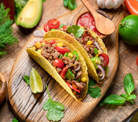 Mexican meat tacos or beef stuffed tortillas and lime slices near them on wooden serving board.
