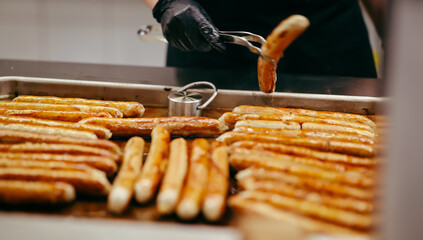 Traditional German sausages being grilled on a large tray in a professional kitchen, flipped by a...
