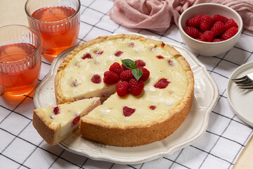 Homemade baked cheesecake with fresh raspberries. Kompot drink in glasses. Beige table with textile runner.