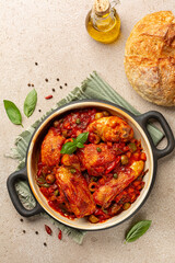 Chicken Cacciatore, Italian hunter style chicken stew made with  vegetables simmered in a tomato sauce with wine and herbs, olives and capers. Fresh bread. Top view, vertical image.