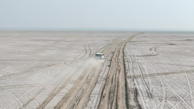 Aerial drone shot following a white vehicle traversing the surreal, empty landscape of the Rann of Kutch.