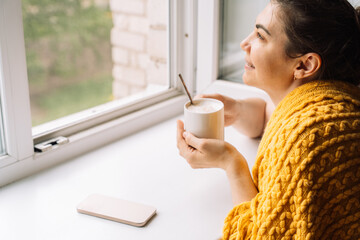 Woman smiling while holding coffee and looking out the window, enjoying tech-free time. High quality photo