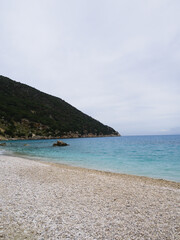 Obraz premium White gravel beach under cloudy sky in Kefalonia with clean coastline, perfect for commercial use and copyspace.