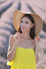 Beautiful young girl in yellow dress and hat in purple lavanli field in summer at sunset