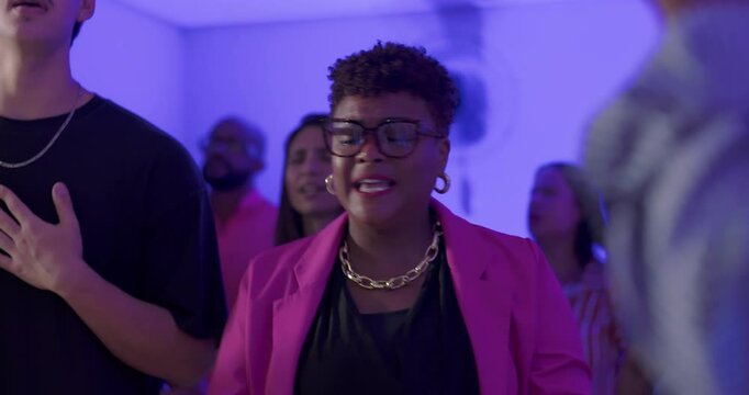 African American woman with short hair leading evangelical worship with microphone, surrounded by congregation with raised hands and prayerful expressions
