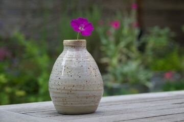 Hand-made ceramic bud vase with single dark pink geranium flower.