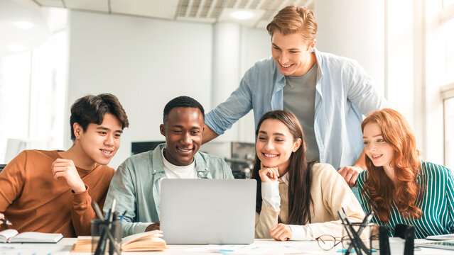Studying Together. Group of diverse multiracial students sitting at desk in auditorium using laptop, watching tutorial or educational video, doing research and making project for college