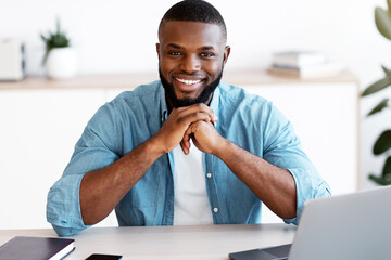 Portrait of smiling african american entrepreneur sitting at desk in home office, handsome black...