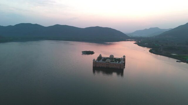 Aerial drone shot of Jal Mahal at sunrise, reflecting softly on the calm lake surface.