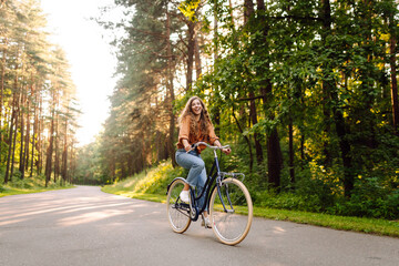 Happy woman riding a bicycle along a path in the forest in the rays of the sun. Beautiful woman...