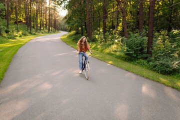 Happy woman riding a bicycle along a path in the forest in the rays of the sun. Beautiful woman...