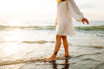 Legs of a young woman walking along the seashore at sunset. Beautiful woman in a dress on the...