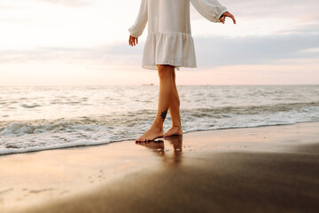 Legs of a young woman walking along the seashore at sunset. Beautiful woman in a dress on the...