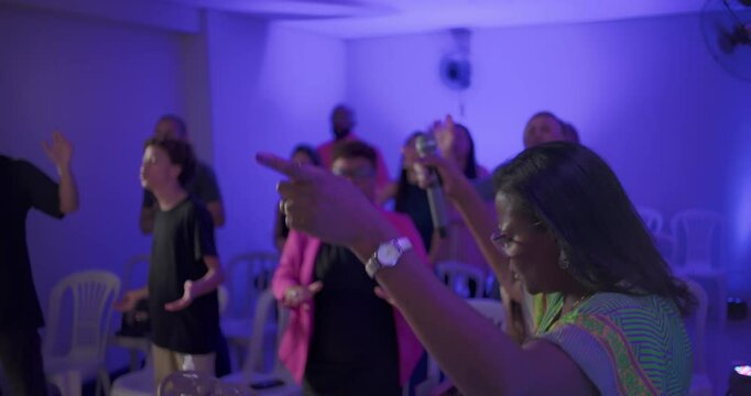 Female worship leader pointing with microphone while leading evangelical church congregation in celebration with hands raised and joyful singing
