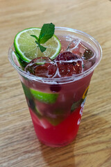 A refreshing strawberry mojito in a clear plastic cup, garnished with fresh lime slices and mint leaves, and filled with ice. A perfect cool beverage for summer or any festive occasion