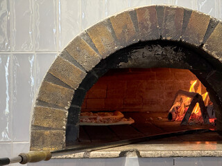 A traditional wood-fired pizza oven with a glowing fire and a pizza baking inside, showcasing...