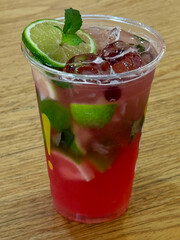 A refreshing strawberry mojito in a clear plastic cup, garnished with fresh lime slices and mint leaves, and filled with ice. A perfect cool beverage for summer or any festive occasion
