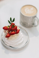 Mini strawberry pavlova with whipped cream and pistachios served beside a latte art coffee in marble mug